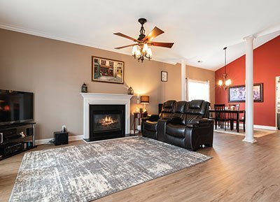 A cozy living room featuring a modern fireplace with a TV on the left. Brown leather recliners and a large area rug add comfort, while white columns separate the spaces. The dining area, with red accent walls and a chandelier, is visible in the background—ideal inspiration for those considering home remodeling contractors.