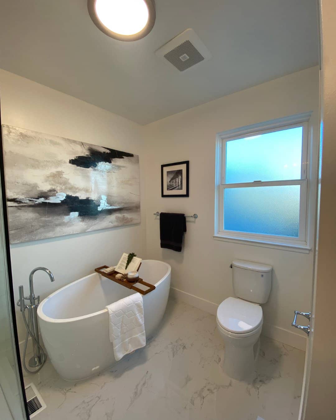 Close-up of a detailed bath caddy with a ceramic cup, a smooth river stone, and a book over a free-standing soaking tub in a modern San Carlos master bathroom remodel by Genuine Kitchen & Bath