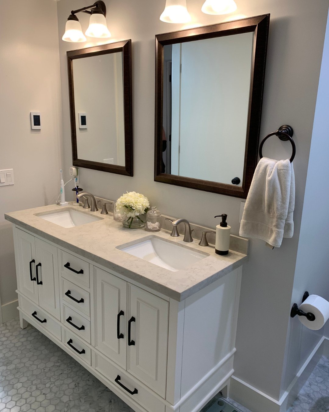 Modern bathroom remodel in San Carlos, CA featuring a white double vanity, black hardware, and marble-look countertops.