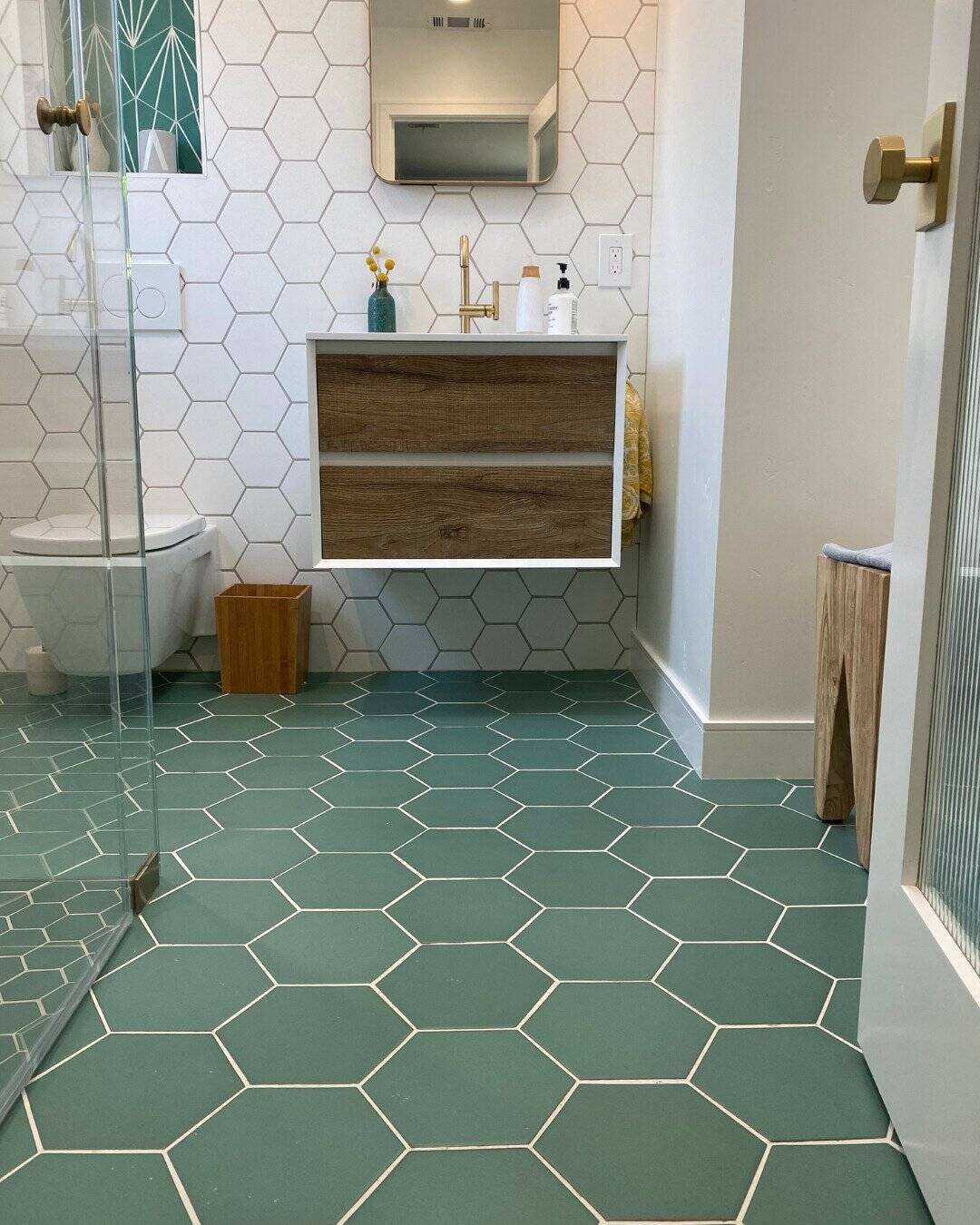Modern bathroom remodel in San Carlos, CA featuring teal green and white hexagonal floor and wall tiles, a floating wood vanity with gold fixtures, and a wall-mounted toilet