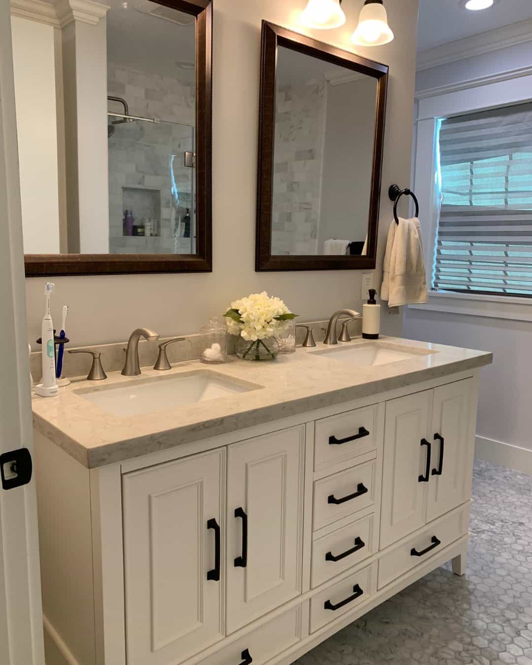 A modern bathroom remodel in San Carlos, CA by Genuine Kitchen and Bath, featuring a white double vanity with matte black hardware, marble countertops, and a gray and white hexagonal tile floor