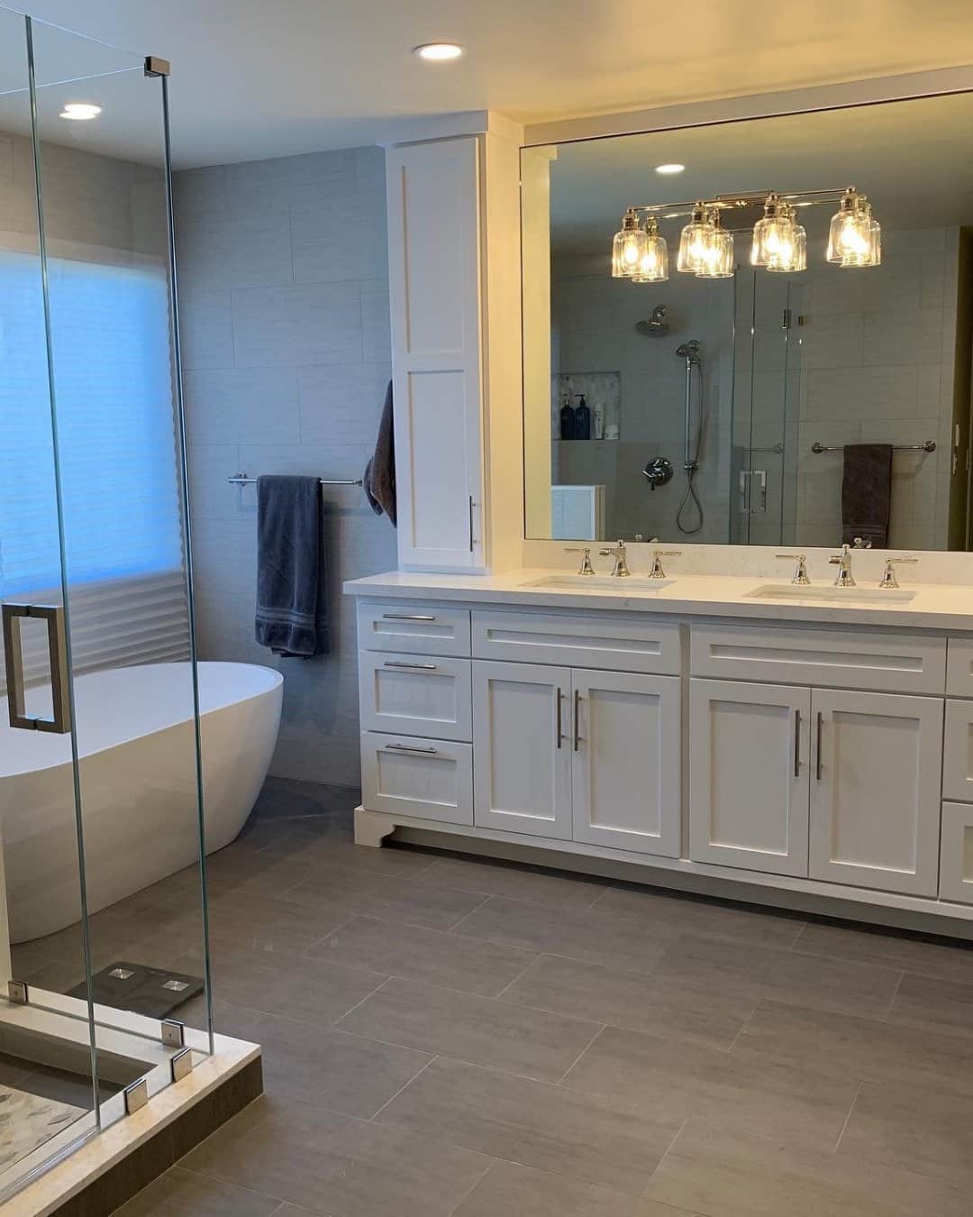 A comprehensive view of a modern master bathroom remodel in San Carlos, CA, by Genuine Kitchen and Bath, featuring a large white freestanding soaking tub, a walk-in glass shower enclosure, and a spacious double vanity with white cabinets and modern light fixtures