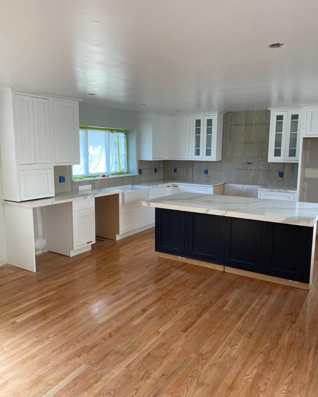 Kitchen renovation in progress in San Carlos, CA by Genuine Kitchen and Bath, featuring white shaker cabinets, a large navy blue island with marble-style quartz countertops, and hardwood floors